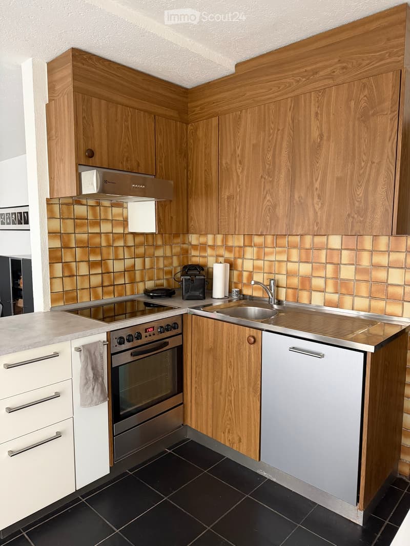 Modern kitchen with wooden cabinets, stainless steel appliances, and black tiled floor.