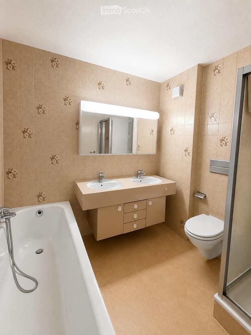 Modern bathroom with beige tiles, a large mirror, a double sink vanity, a bathtub, and a toilet.