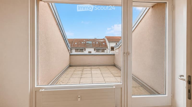 Balcony with tiled floor, white walls, and a view of neighboring buildings and rooftops.
