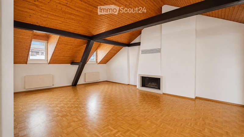 Empty room with wooden flooring, white walls, exposed wooden ceiling beams, and a built-in fireplace.