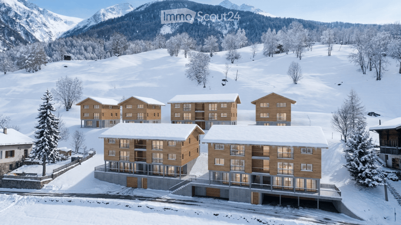 A cluster of modern wooden apartment buildings in a snowy mountain landscape, surrounded by trees and snow-covered slopes.