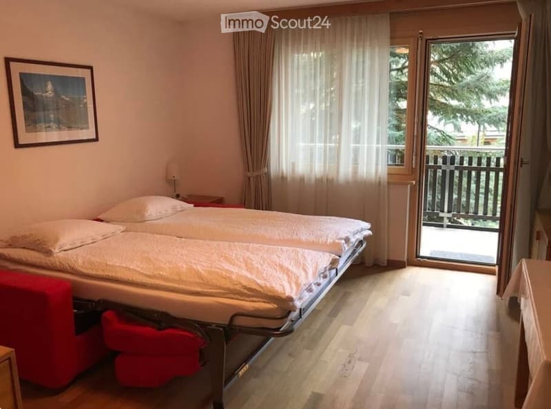 Cozy bedroom with a double bed, nightstand, lamp, and a large window with a view of the balcony.