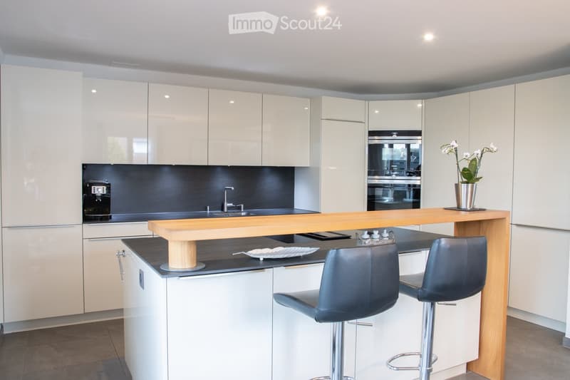Modern kitchen with white cabinets, a wooden island, two bar stools, a coffee maker, and a vase with flowers on the island.