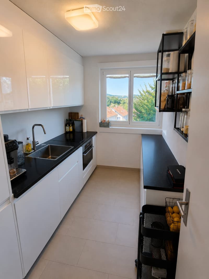 Modern kitchen with white cabinets, black countertops, stainless steel sink, and a window overlooking a scenic view.