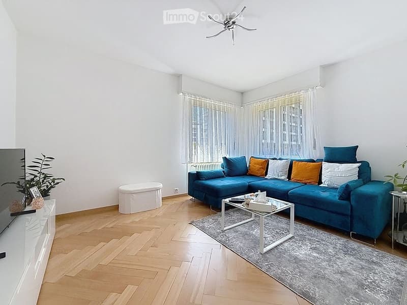 Modern living room with a blue sectional sofa, colorful throw pillows, a glass coffee table, a TV stand, and a small plant in the corner.