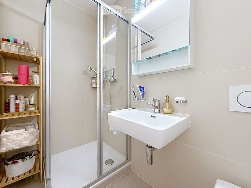 Modern bathroom with a white sink, mirror cabinet, glass-enclosed shower, and wooden shelf holding towels and toiletries.