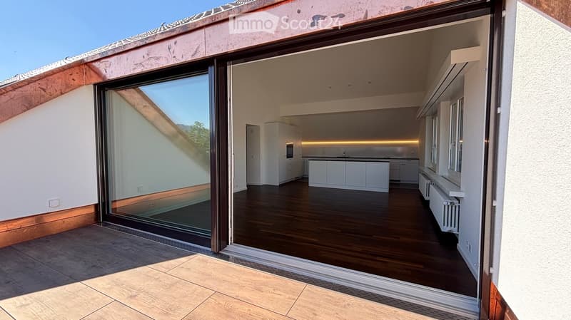 Modern kitchen with white cabinets, a central island, and a sink, connected to a tiled outdoor area through large glass doors.