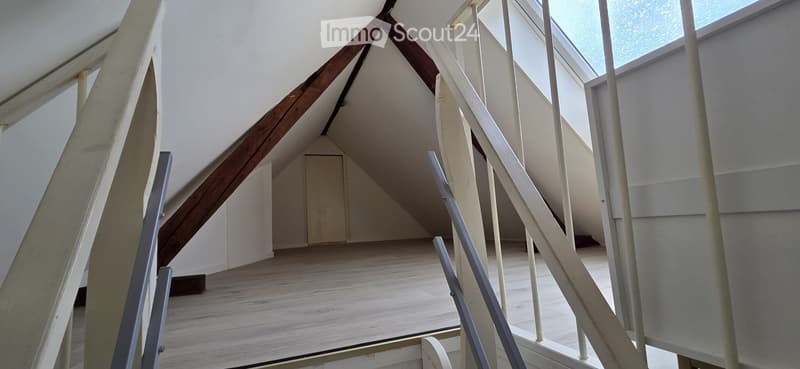 Empty attic space with wooden floor, exposed wooden beams, and skylight windows.