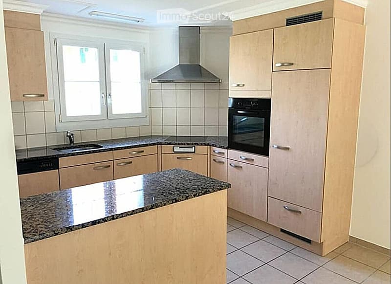 Modern kitchen with light wood cabinets, granite countertop, stainless steel appliances, and a central island.