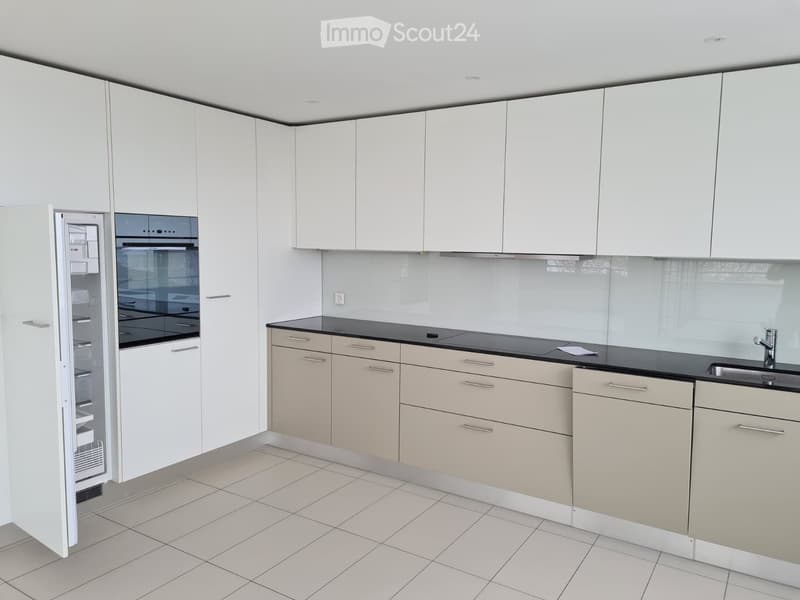 Modern kitchen with white cabinets, beige lower cabinets, black countertops, and stainless steel appliances including a refrigerator and oven.
