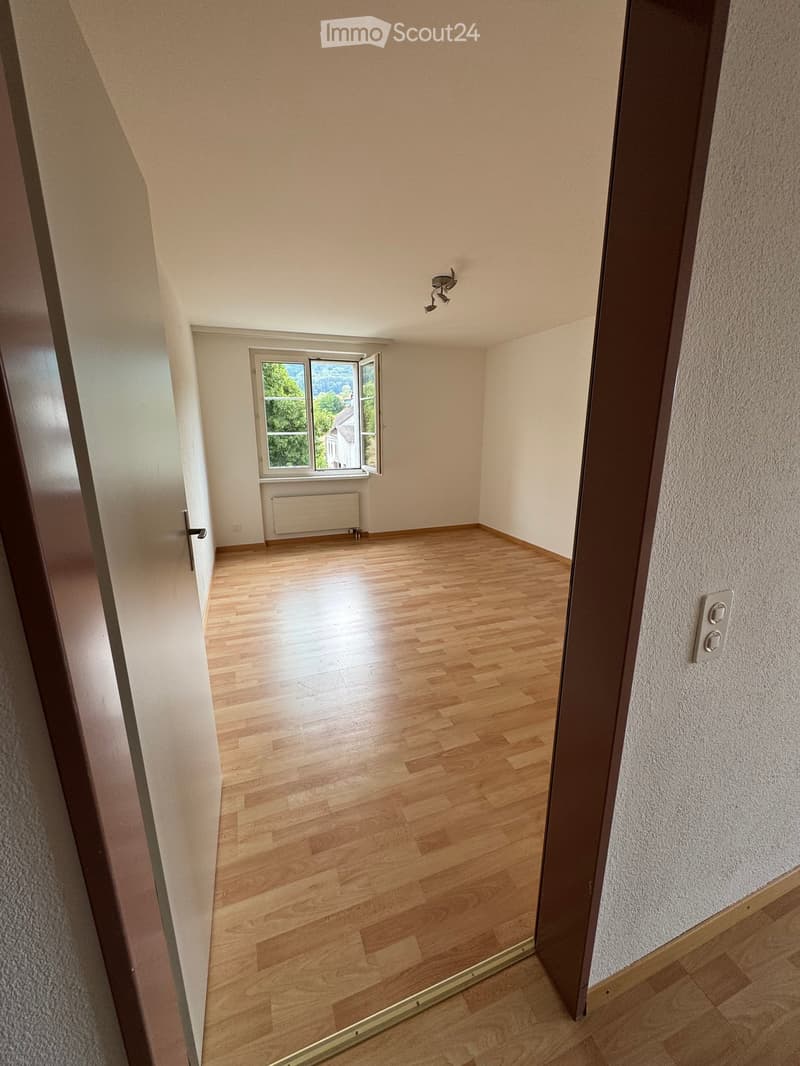 Empty room with wooden flooring, white walls, and a window with a radiator below it. The room is brightly lit with natural light coming through the window.