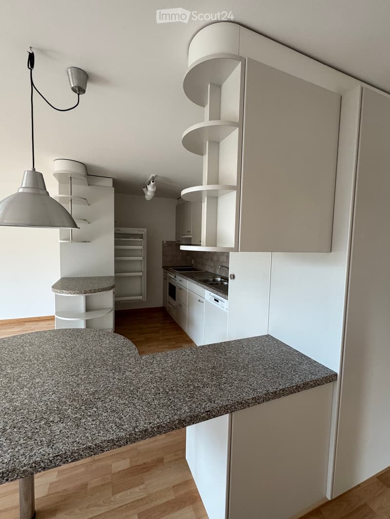Modern kitchen with white cabinets, granite countertops, and stainless steel appliances including a sink, oven, and dishwasher. Pendant lights hang above the island.