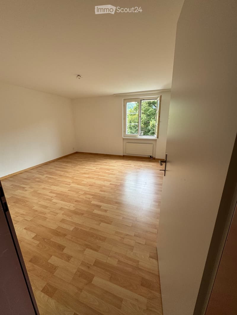 Empty room with wooden flooring, white walls, and a window with a view of greenery. No furniture or equipment is present.