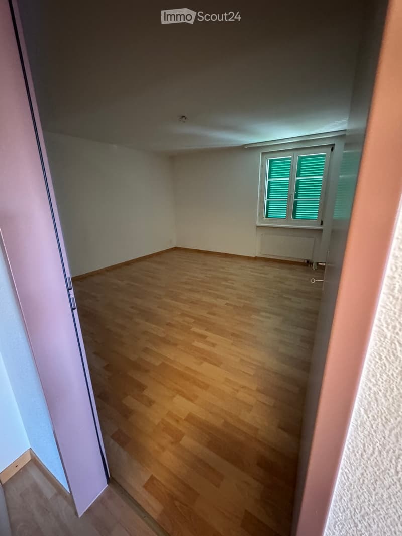 Empty room with wooden flooring, white walls, and a window with green shutters. No furniture or equipment is present.