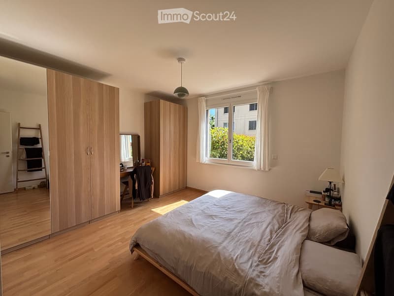Modern bedroom with wooden flooring, large bed, built-in wardrobes, desk, and nightstand.