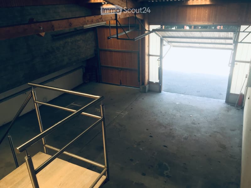 Empty garage with concrete floor, wooden walls, metal staircase, and large open doorway leading outside.