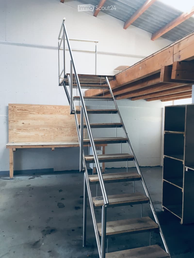 Empty room with unfinished wooden stairs, metal railings, and exposed wooden beams on the ceiling. Bare walls and concrete floor.