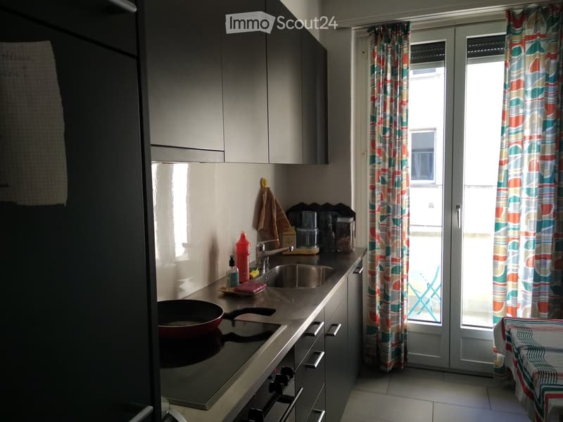 Modern kitchen with stainless steel sink, oven, and cabinets. A colorful curtain covers the window, and a bottle is placed on the counter.