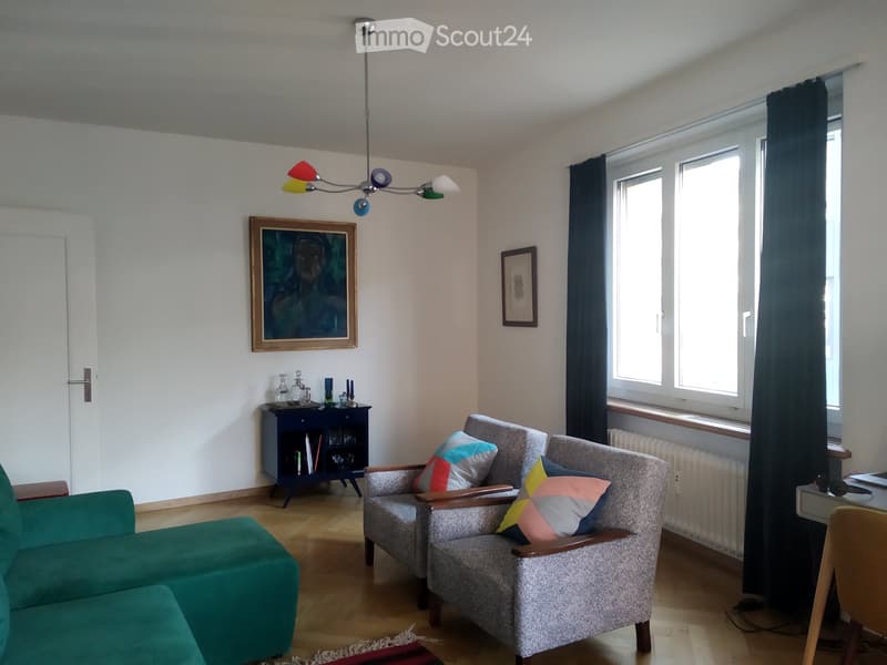 Living room with a green sofa, two armchairs, a small table, a cabinet, and colorful pillows.