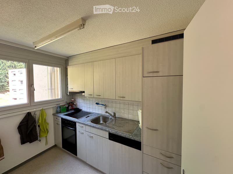 Modern kitchen with light wood cabinets, stainless steel sink, oven, and dishwasher. Countertop has a few cleaning supplies and a dish rack.