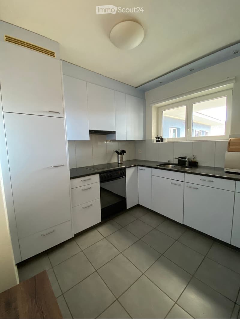 Modern kitchen with white cabinets, stainless steel sink, and black countertop. Features include a built-in oven, stove, and tiled floor.