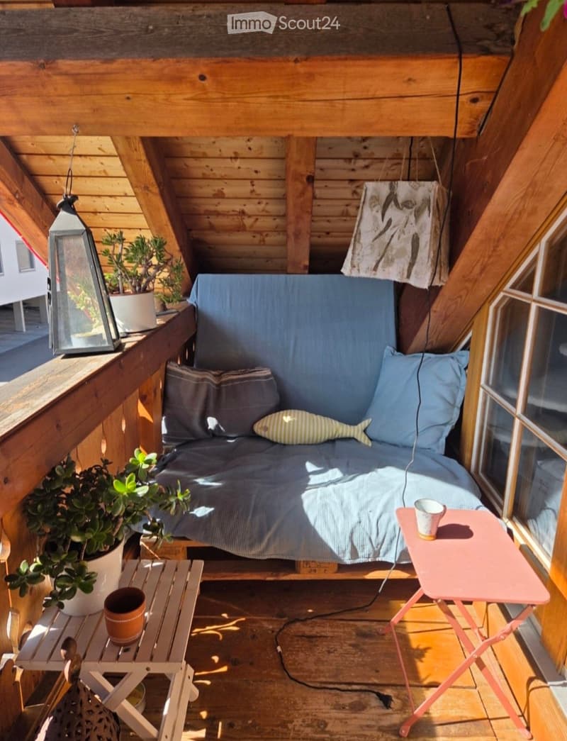 Cozy wooden balcony with a small sofa, two side tables, potted plants, and a lantern.