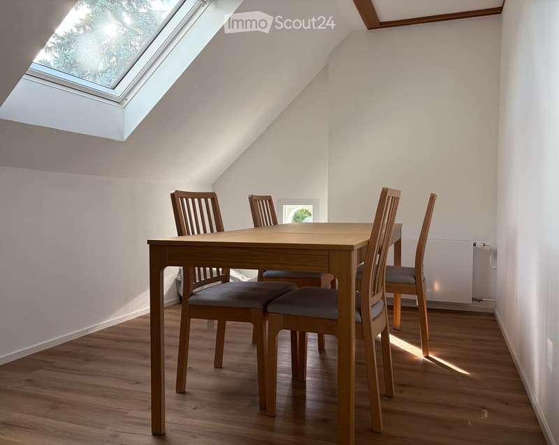 Bright attic dining area with wooden dining table and four chairs, skylight window, wooden flooring, white walls.