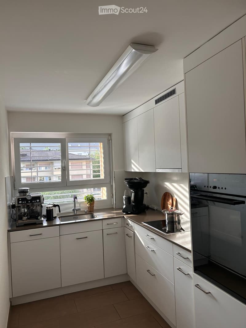 Modern kitchen with white cabinets, stainless steel appliances, and a window overlooking a residential area.