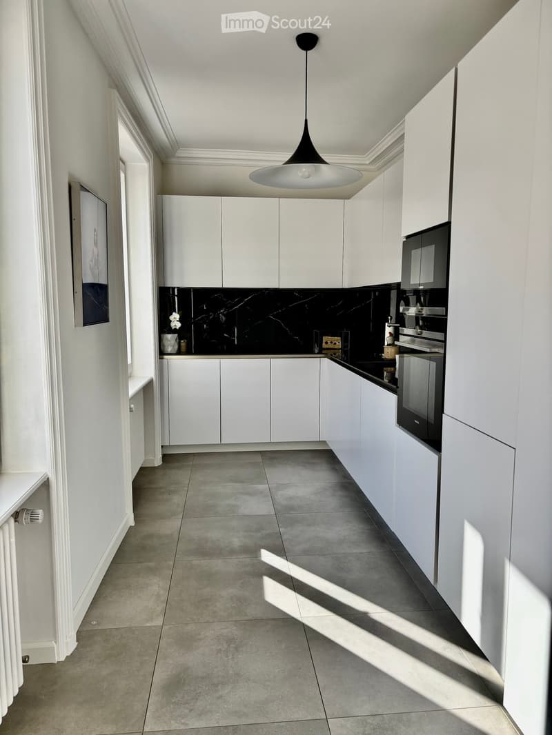Modern kitchen with white cabinets, black backsplash, grey tiled floor, and a pendant light fixture.