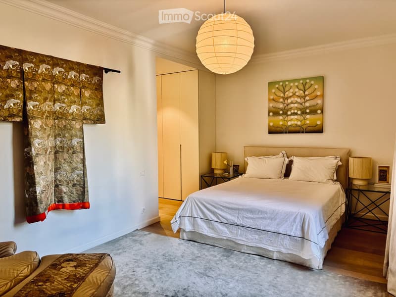 Elegant bedroom with a large bed, nightstands, lamps, a patterned chair, and a painting on the wall.