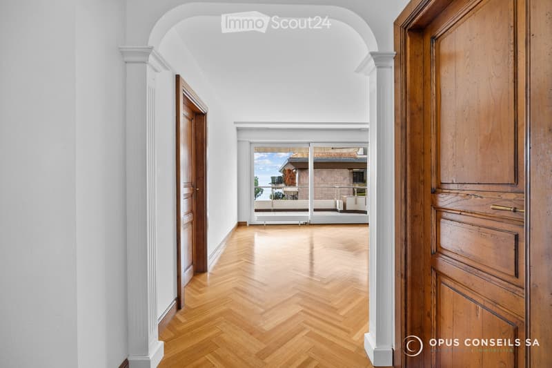 Elegant hallway with herringbone wooden flooring, white walls, and arched doorways leading to a balcony area with outdoor seating.
