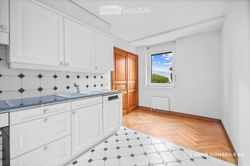 Modern kitchen with white cabinets, a blue countertop, a sink, and a dishwasher. The room features wooden flooring and a window offering a scenic view.