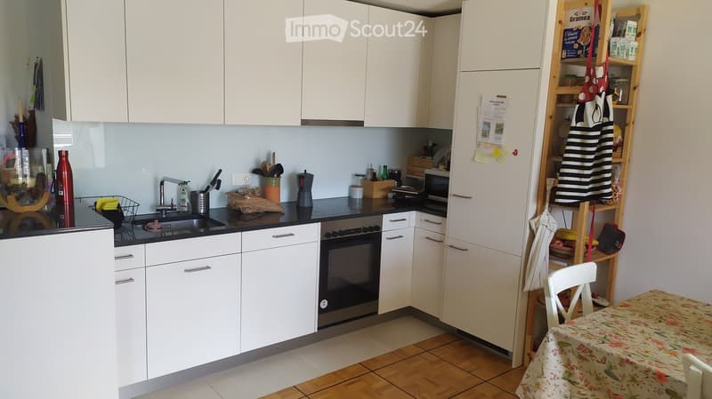 Modern kitchen with white cabinets, black countertops, and stainless steel appliances. Includes a sink, faucet, oven, refrigerator, and a small dining area with a table and chair.