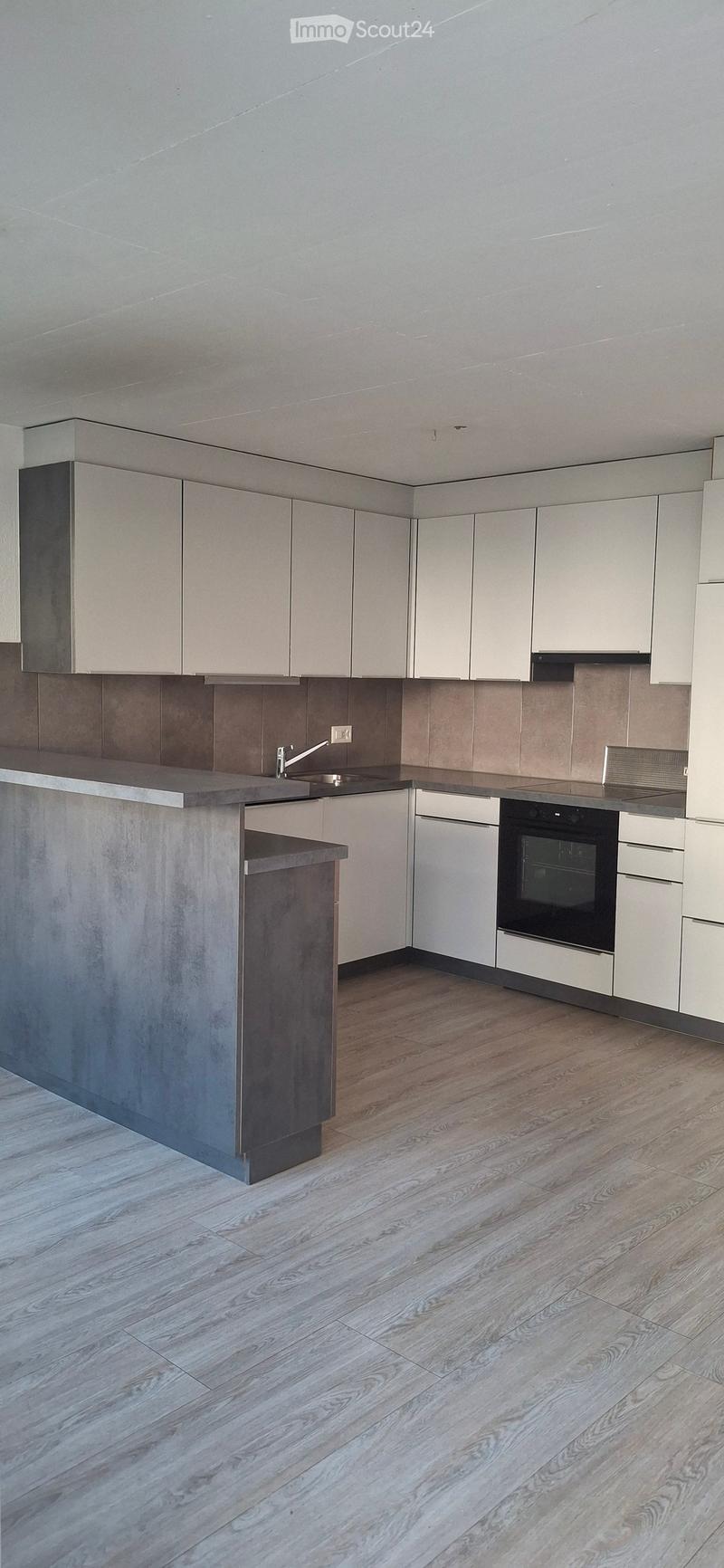 Modern kitchen with light grey cabinets, a central island, and wooden flooring. Features include a sink, faucet, oven, and dishwasher.