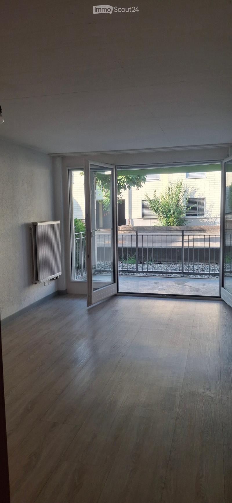 Empty room with wooden flooring, white walls, and large sliding glass doors leading to a balcony area with a metal railing and outdoor space.