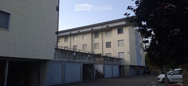Modern multi-story building with a raised ground floor, garage, and parking area.