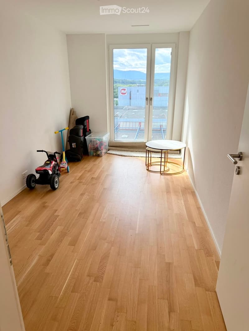 A small, well-lit hallway with wooden flooring, a round white table near the door, and a few items including a scooter, toy car, and luggage stacked against the wall.