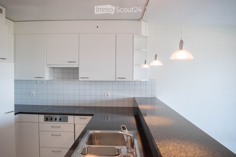 Modern kitchen with white cabinets, stainless steel sink, pendant lights, and a dark countertop.