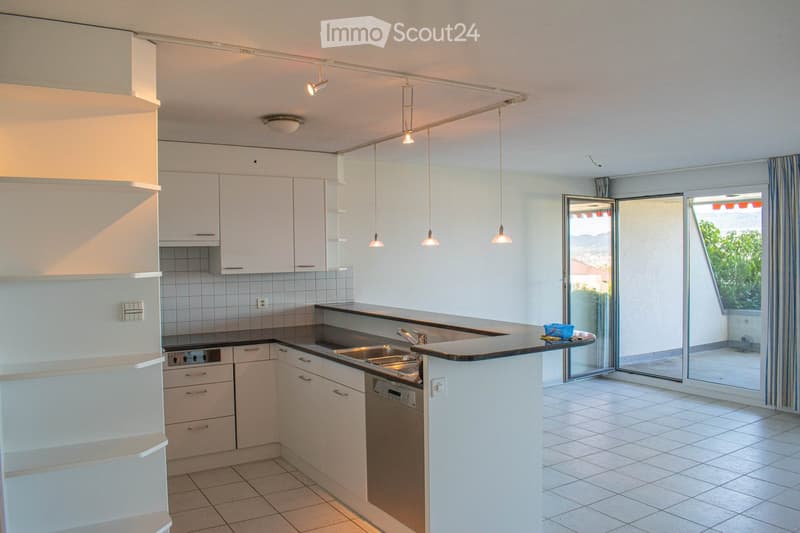 Modern kitchen with white cabinets, stainless steel sink, dishwasher, and pendant lights. Features a large window with striped curtains and a view of the outdoor area.