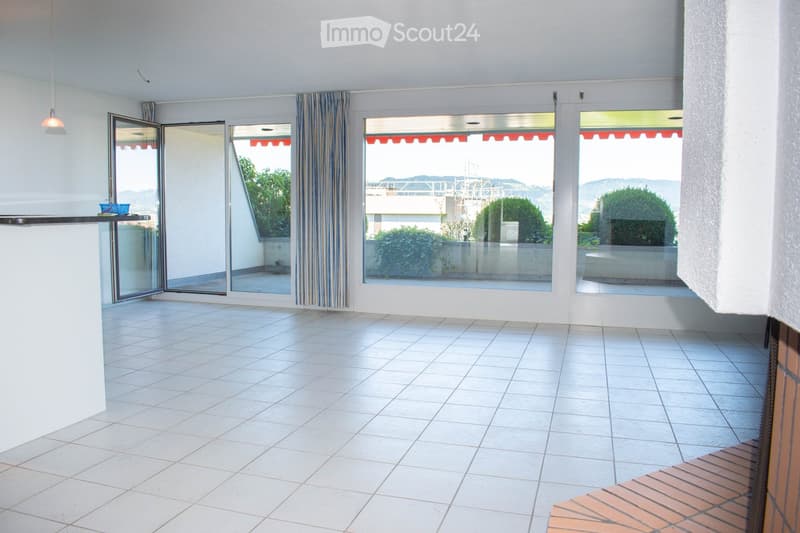 Empty room with white tiled floor, large glass sliding doors leading to a balcony, white walls, and a small counter with a blue basket on it.