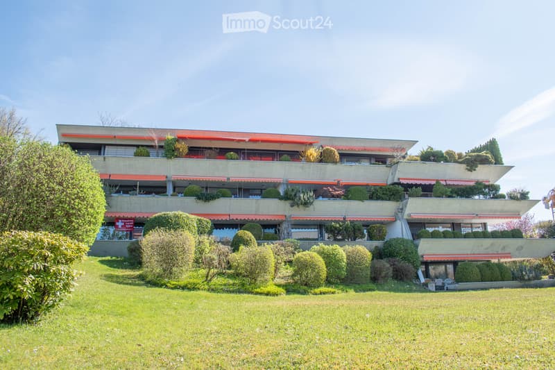 multi-story building, red awnings, multiple balconies, green plants, large lawn