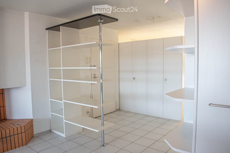 Empty room with white tiled floor, white walls, built-in white cabinets, and a tall white shelving unit with glass shelves.