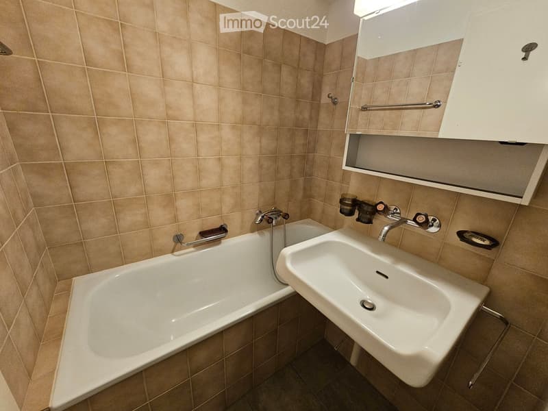 Bathroom with beige tiled walls, a bathtub, a sink, a mirror, and a faucet.