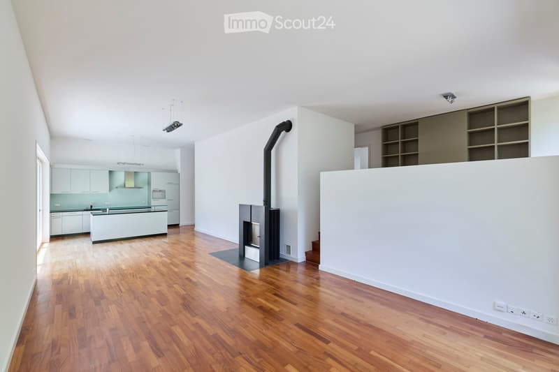 Open-plan living and kitchen area with wooden flooring, modern kitchen cabinets, a central island, and a fireplace with a chimney.