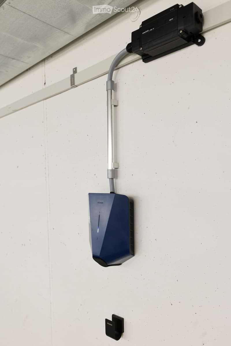 A modern light fixture mounted on a white wall with a cable running down to a base unit.