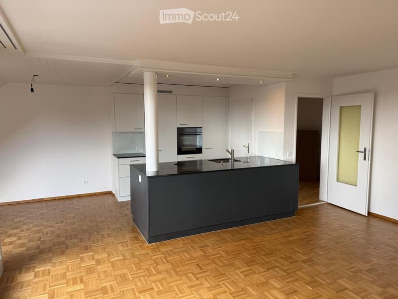 Modern kitchen with white cabinets, dark island, wooden flooring, and built-in appliances.