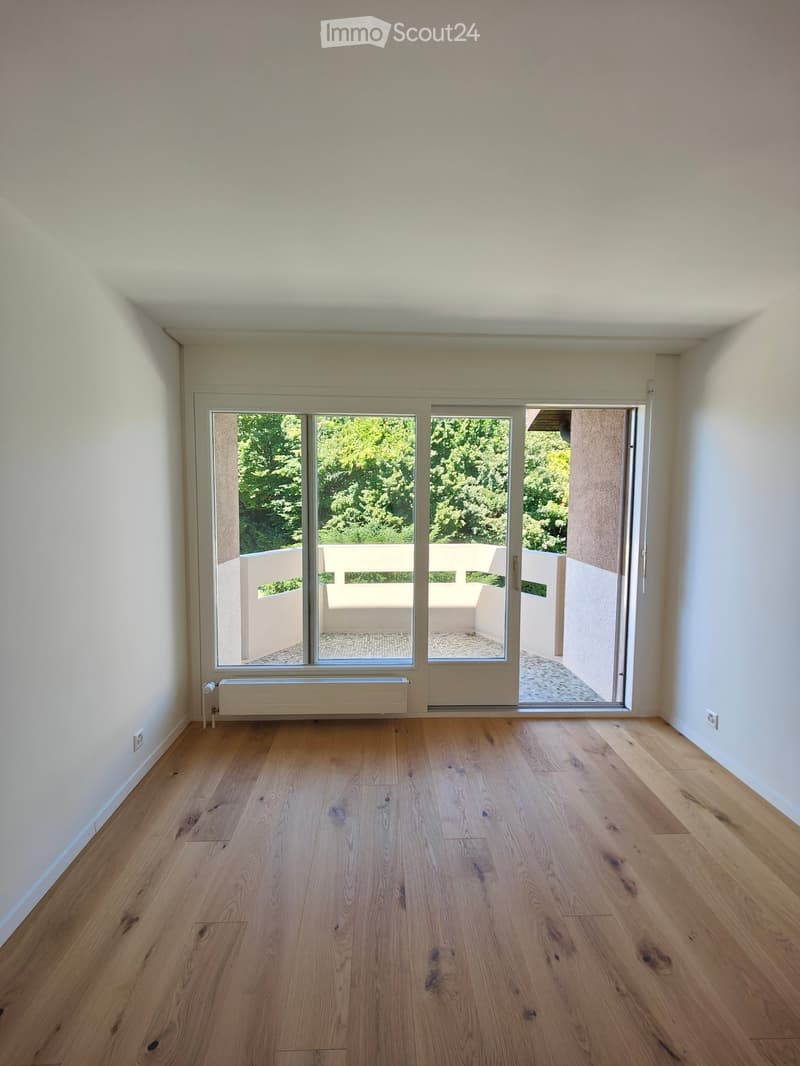 Empty room with light wooden flooring, white walls, large sliding glass doors leading to a balcony, and a radiator under the window.