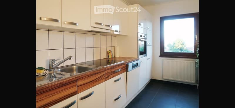 Modern kitchen with white cabinets, wooden countertops, stainless steel sink and faucet, built-in oven and dishwasher, and a window overlooking greenery.