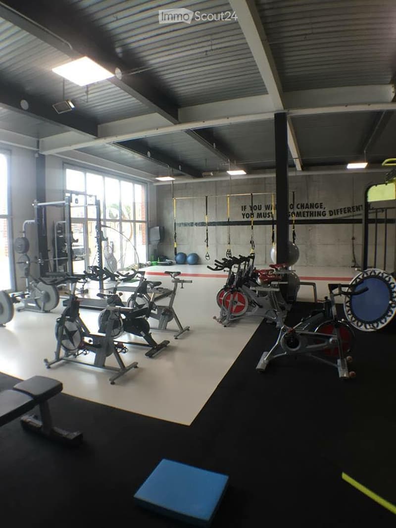 Modern gym with multiple exercise bikes, weight benches, and weights. Large windows provide natural light, and motivational quotes are displayed on the walls.