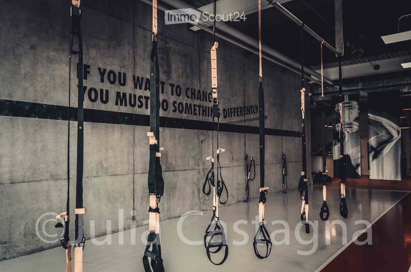 Modern fitness studio with wooden and black suspension trainers hanging from the ceiling, motivational quote on the wall, polished concrete floor.